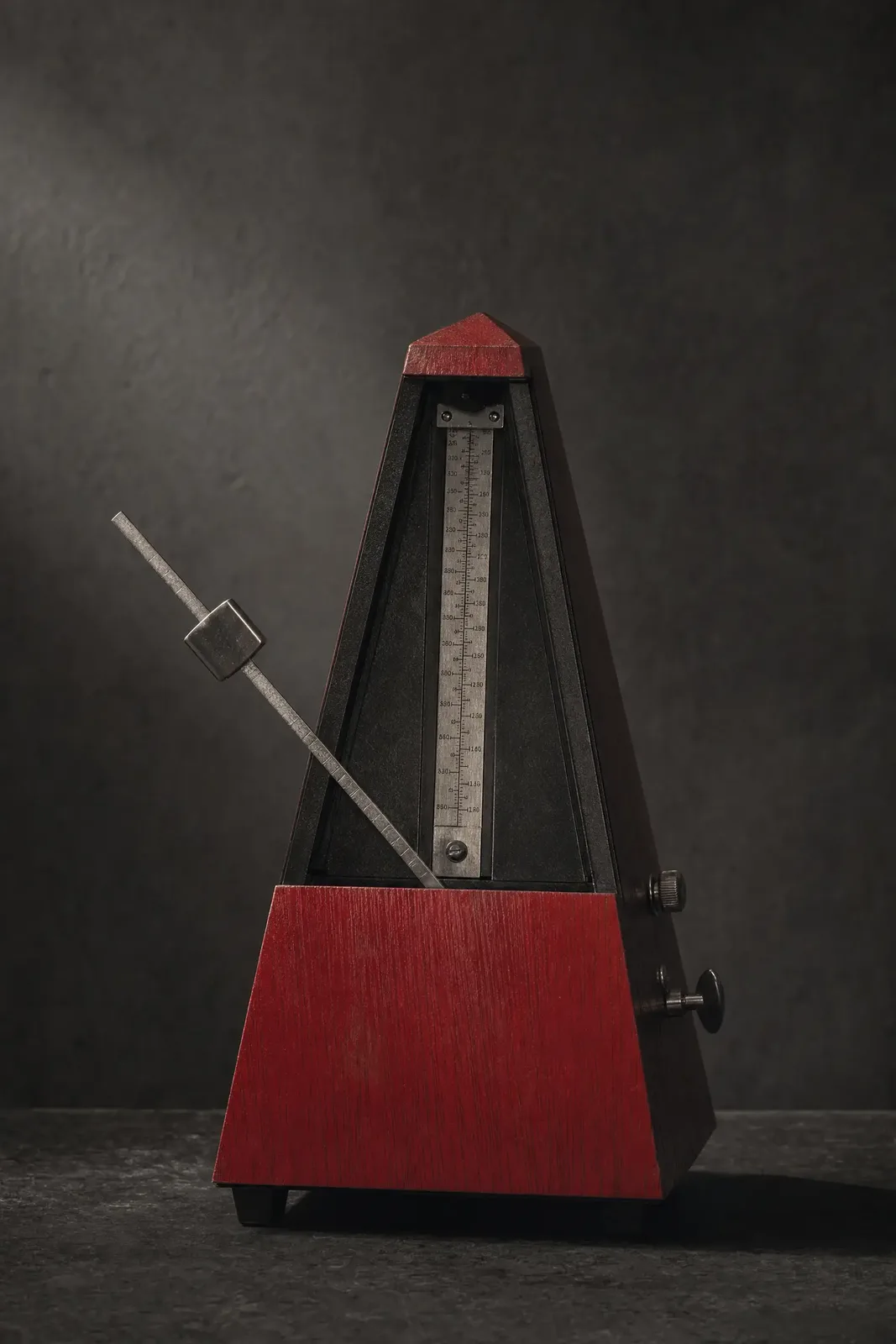 A red wooden metronome with its pendulum swung wide, weight set low for a slow tempo